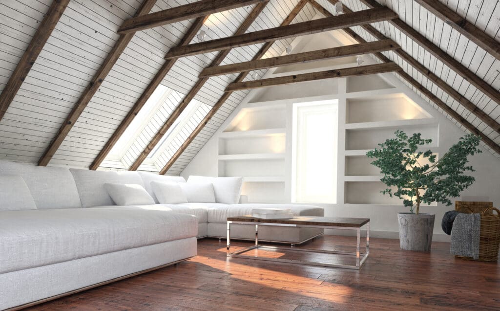 A bright attic living room showcases exposed wooden beams, white walls, built-in shelves, and a large white sectional sofa—perfect inspiration for your next attic renovation or loft conversion project.