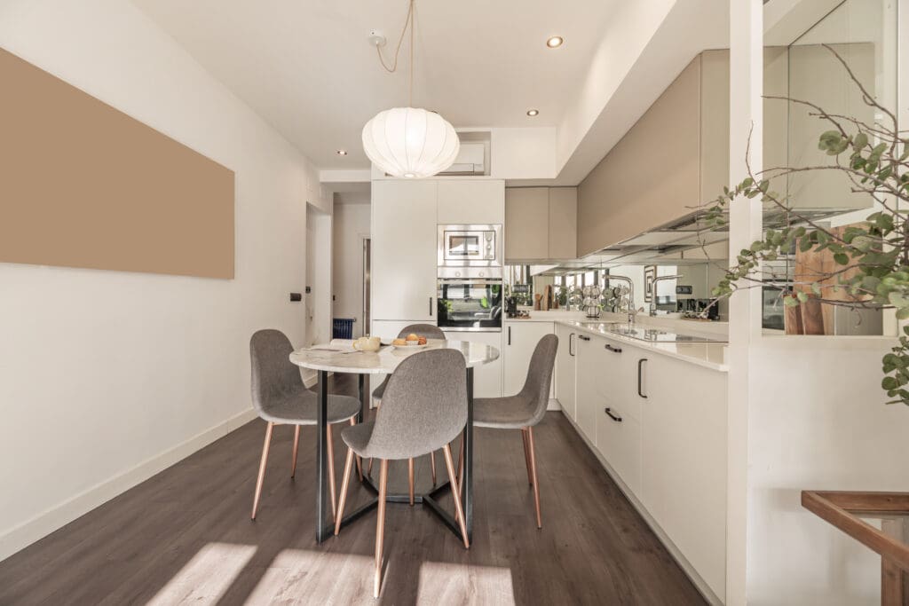 Modern kitchen and dining area with white cabinets, a round marble table, four grey chairs, wooden floors, and a large paper lantern light fixture—ideal for those seeking inspiration for home extensions or house extensions.