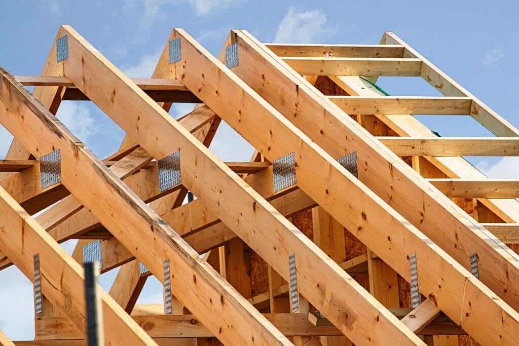 Close-up view of wooden roof trusses under construction against a blue sky, highlighting skilled carpenters' craftsmanship and the precision of woodworking in a building in progress.